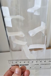 Close-up photo of a clear acrylic pipe with strips of adhesive hook tape stuck as flaps in various places down the pipe.